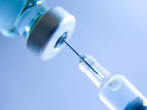 Syringe entering bottle blue background