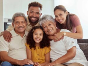 Portrait of mixed race family with child enjoying weekend in living room at home. Adorable smiling hispanic girl bonding with grandparents, mother and father. Happy couples and child sitting together