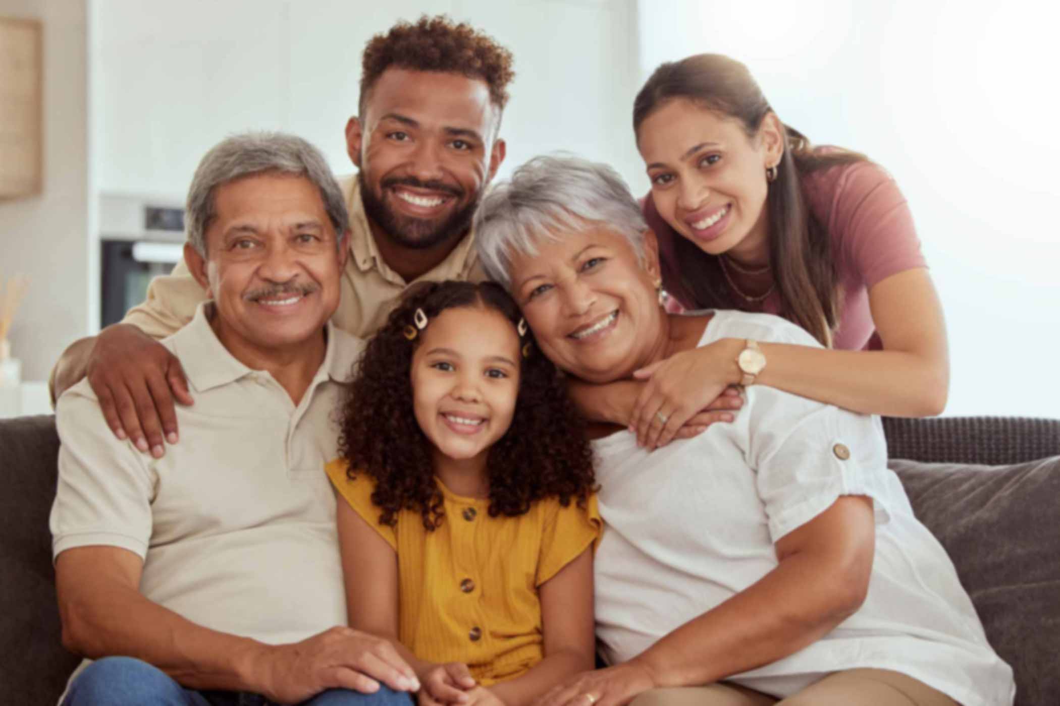 Age-Specific-Care-for-CNAs Portrait of mixed race family with child enjoying weekend in living room at home. Adorable smiling hispanic girl bonding with grandparents, mother and father. Happy couples and child sitting together