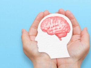 Hands holding a paper cutout of a human face showing the brain